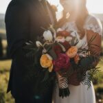 Close-up of a bride and groom embracing, holding a bouquet, against an Italian sunset